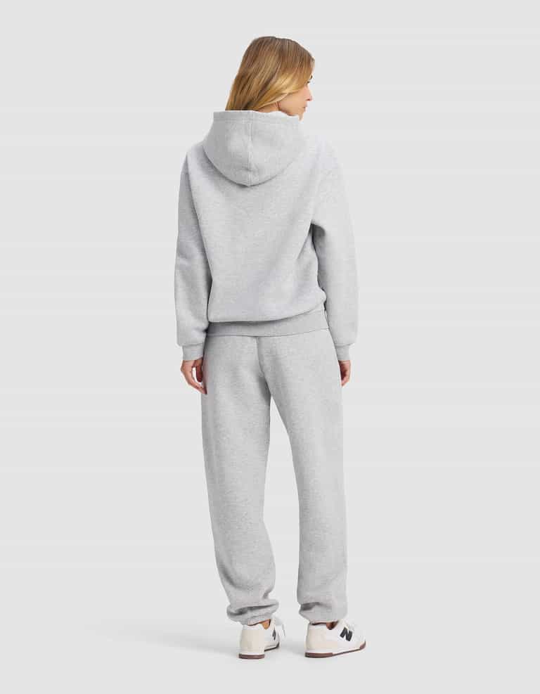 A woman with blonde hair, seen from behind, wears the Cozy Earth Women's Cityscape 2.0 Hoodie & Sweatpant Set in light gray with white sneakers against a plain light gray background.|Color:Heather Grey