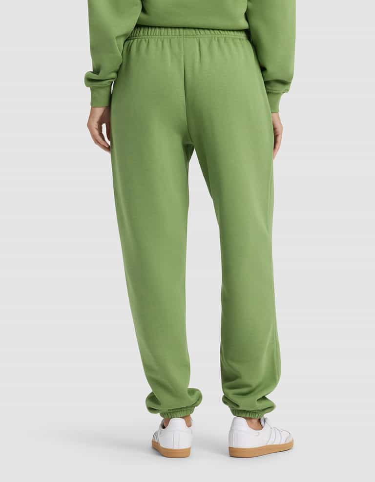 A woman is seen from behind in Cozy Earth's Women's Cityscape 2.0 Sweatpant and a matching green sweatshirt, paired with white sneakers, against a plain background.|Color:Clover