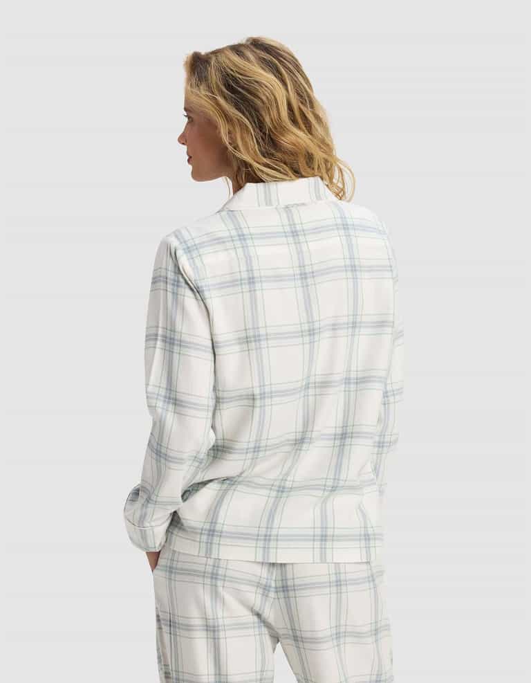 A woman with wavy blonde hair stands with her back to the camera, wearing Cozy Earth’s Women's Farmhouse Long Sleeve Pajama Top in white with light blue and green plaid, set against a plain light grey background.|Color:Wintergreen Plaid