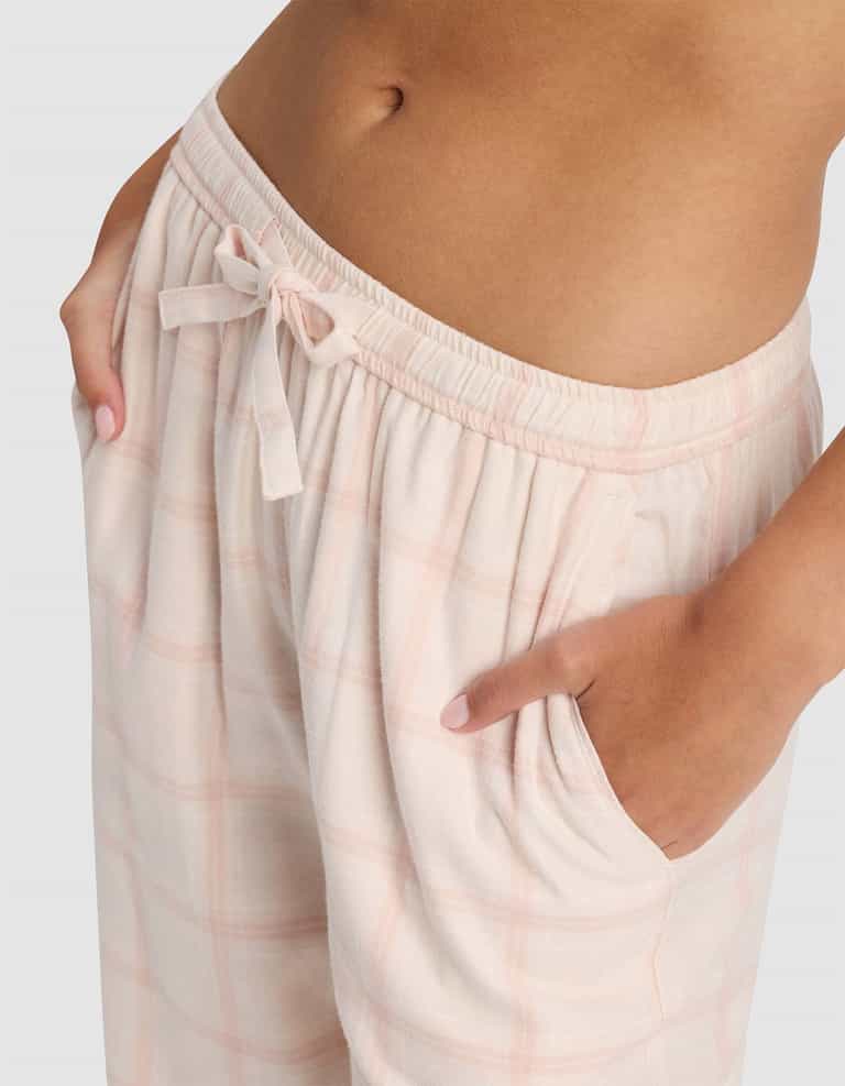 A close-up of a person wearing Cozy Earth Women's Farmhouse Pajama Pant in light pink plaid, featuring a drawstring waist, pockets, and a glimpse of their bare midriff.|Color:Quartz Plaid