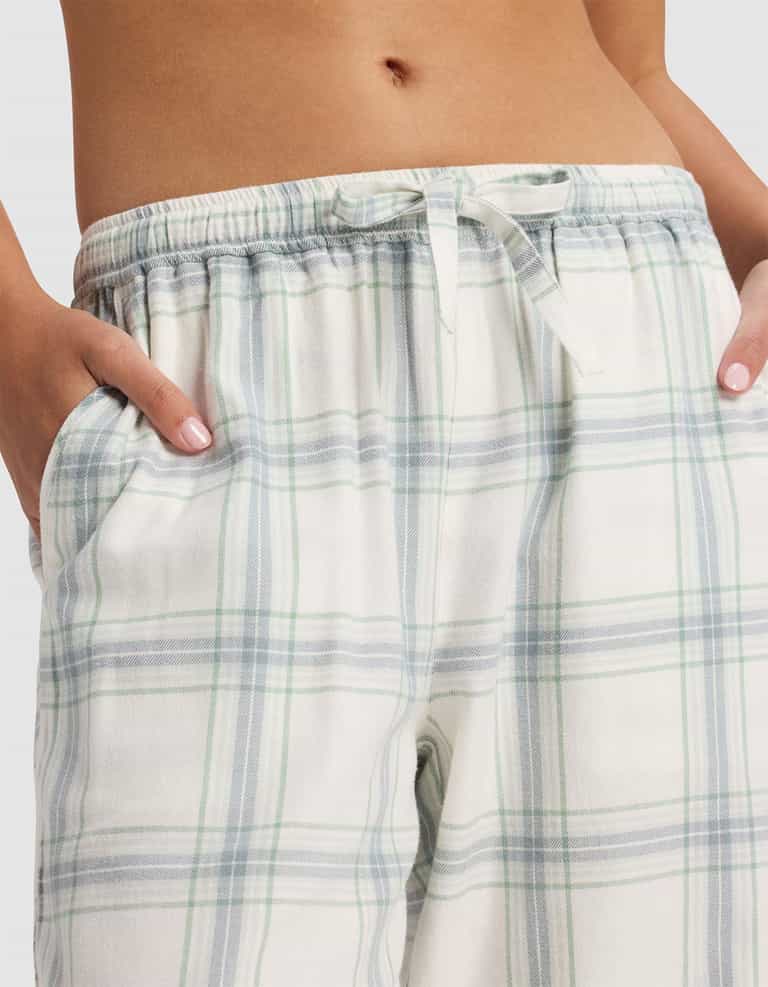 A close-up of a person wearing Cozy Earth Women's Farmhouse Pajama Pant, featuring a soft blue and green plaid pattern, drawstring waistband, and pockets, with the midriff visible.|Color:Wintergreen Plaid