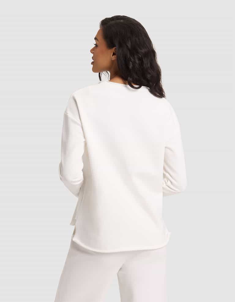 A woman with medium-length dark hair is seen from behind wearing Cozy Earth's Women's Chelsea Pullover in white, paired with white pants, standing against a plain light gray background. |Color:Bone