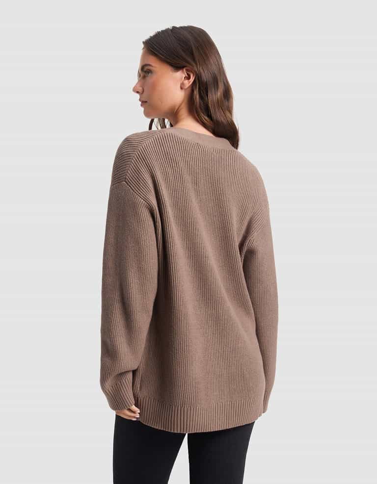 A woman with long brown hair is wearing Cozy Earth's Oversized Classic Cardigan in brown, paired with black pants, and is standing with her back to the camera against a plain light gray background.|Color:Ebony