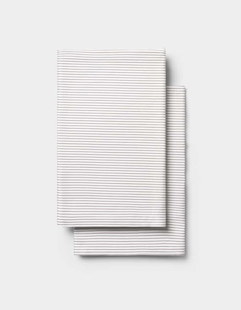Two neatly folded Cozy Earth Bamboo Pillowcases, white with thin horizontal gray stripes, stacked on a plain light gray background.|Color:Charcoal Pinstripe