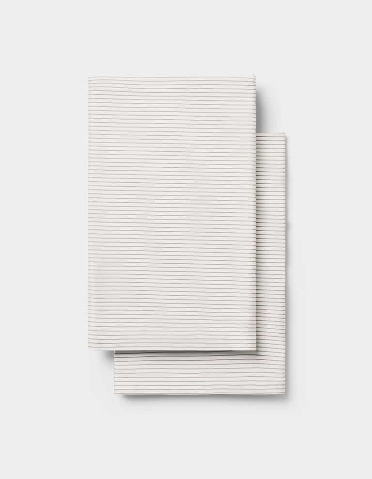 Two neatly folded, light-colored Cozy Earth Bamboo Pillowcases with thin, subtle horizontal stripes, placed one over the other on a plain white background.|Color:Driftwood Pinstripe