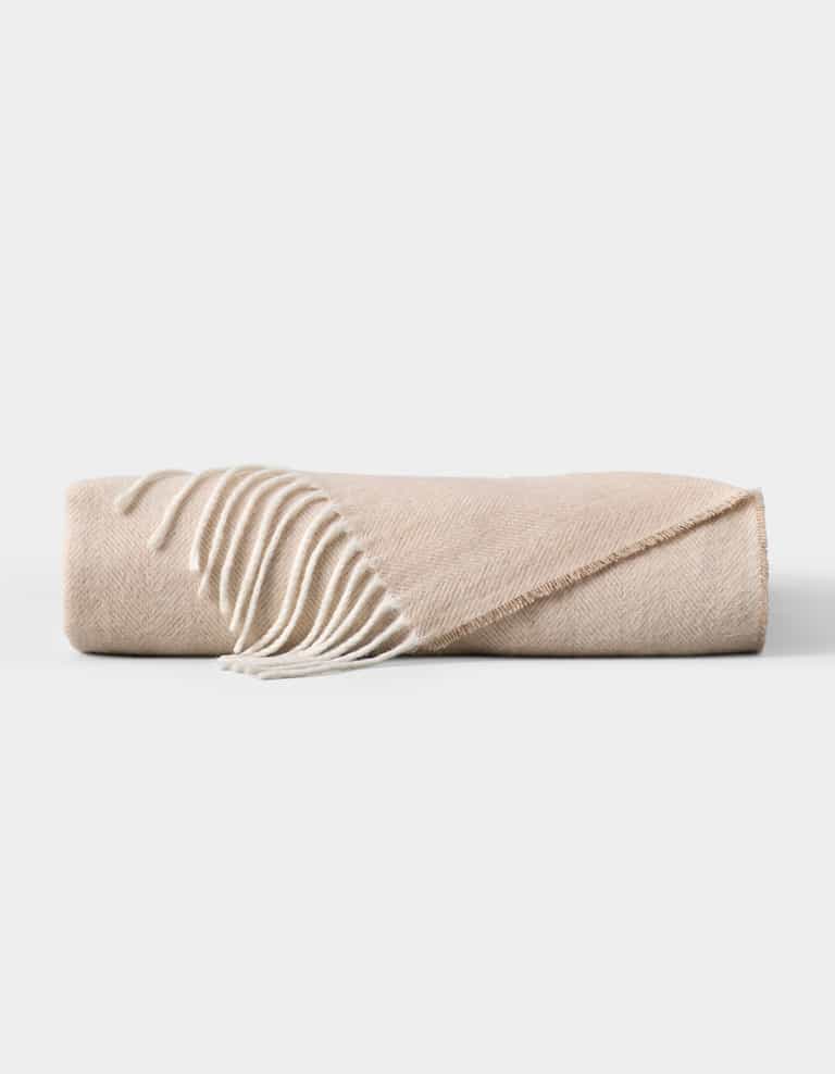 The Cozy Earth Bamboo Herringbone Tassel Throw is a folded beige blanket featuring a subtle herringbone pattern and white tassel fringe on one edge, displayed against a plain white background. |Color:Oatmeal