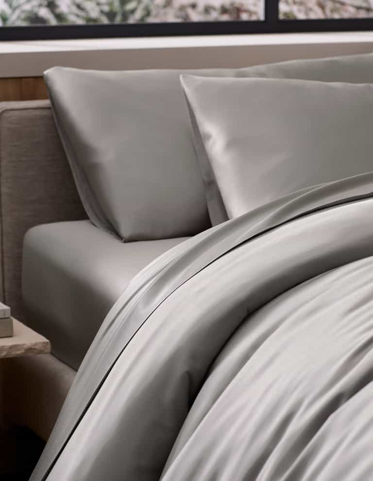 A neatly made bed features the Cozy Earth Bamboo Duvet Cover in light gray with dark trim, paired with matching pillowcases. The bed is near a window with an outdoor view and has a nightstand beside it.