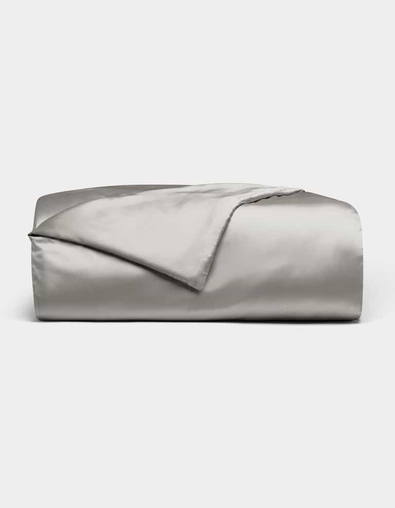A neatly folded Cozy Earth Bamboo Duvet Cover in light gray is displayed against a white background, with one corner turned back to reveal its smooth, shiny fabric.|Color:Light Grey