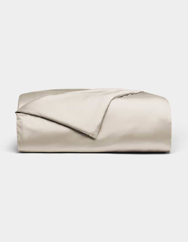 The Bamboo Duvet Cover by Cozy Earth, in light beige with a smooth satin finish, is neatly folded and displayed against a plain white background.|Color:Oat