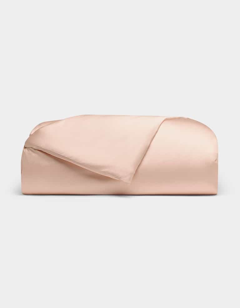 The Cozy Earth Bamboo Duvet Cover, in pale pink, is neatly folded against a plain white background with one corner turned down to reveal its smooth fabric.|Color:Peony