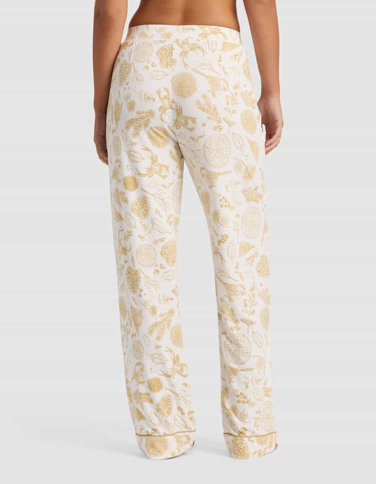 A person models the back view of the Cozy Earth Women's Bamboo Stretch-Knit Pajama Pant, featuring a gold botanical and citrus fruit print on white, shown in a relaxed fit against a plain background.|Color:Winter Toile Dijon