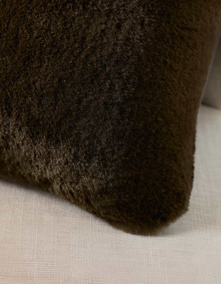 A Cozy Earth Cuddle Pillow in dark brown rests against the back of a light beige, textured fabric sofa.|Color:Espresso |Size:Body