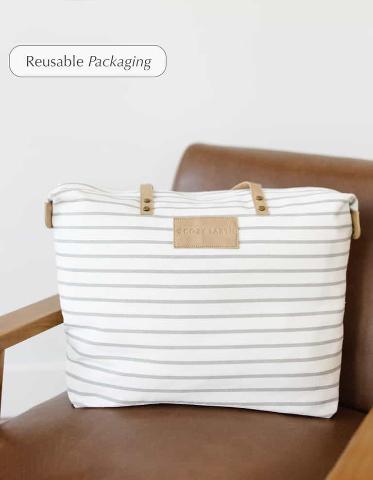 A white and gray striped tote bag with tan handles and a Cozy Earth label, used for the Bamboo Mattress Pad, rests on a brown armchair. "Reusable Packaging" text appears in the top left corner.