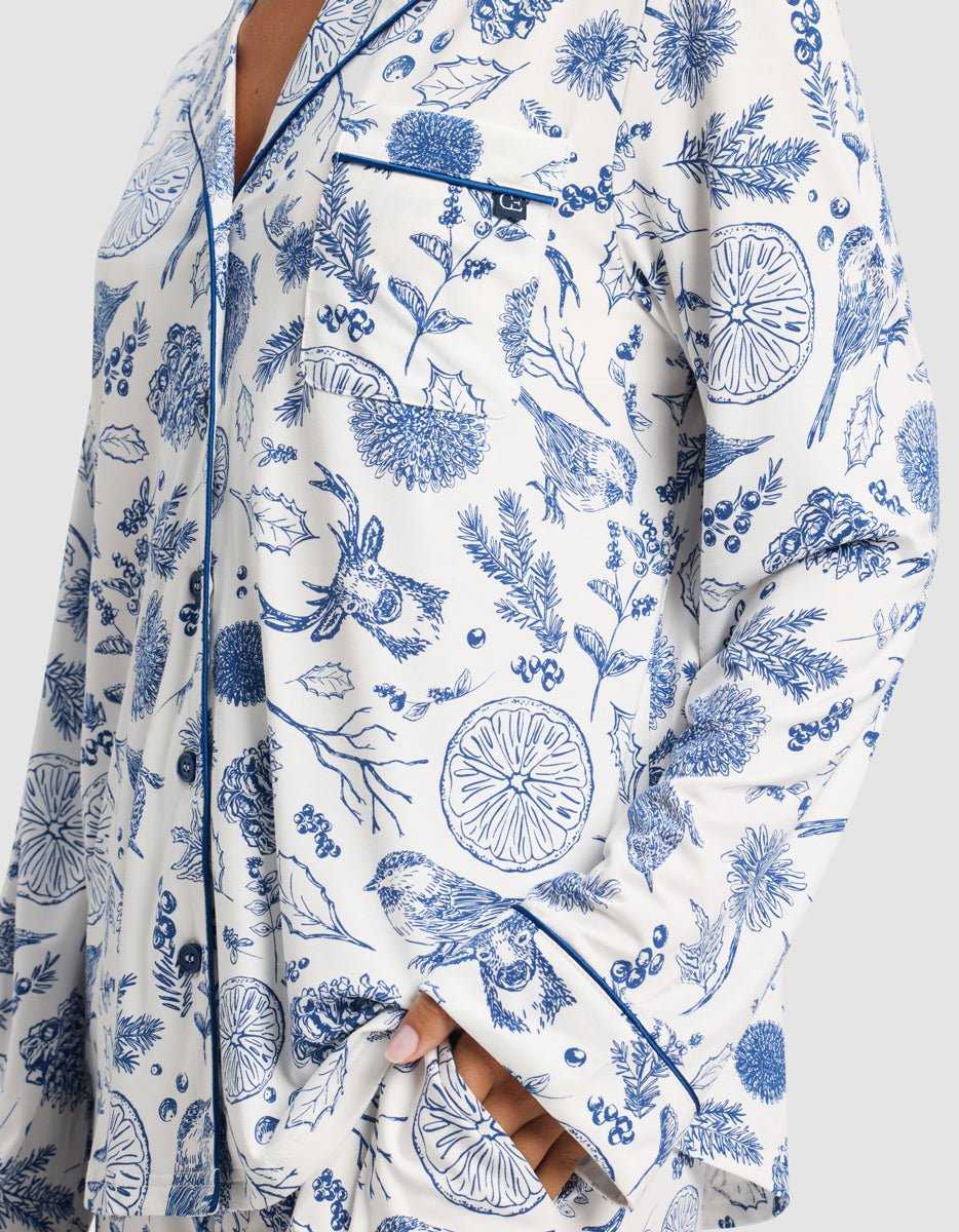 A close-up of a person wearing the Cozy Earth Women's Bamboo Stretch-Knit Long Sleeve Pajama Top in white with blue botanical and animal prints, chest pocket, and navy piping.|Color:Winter Toile Pacific